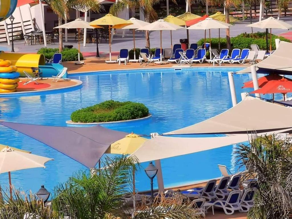 a swimming pool with chairs and umbrellas at قريه اكوا فيو - الساحل الشمالى - الكيلو91 in El Alamein