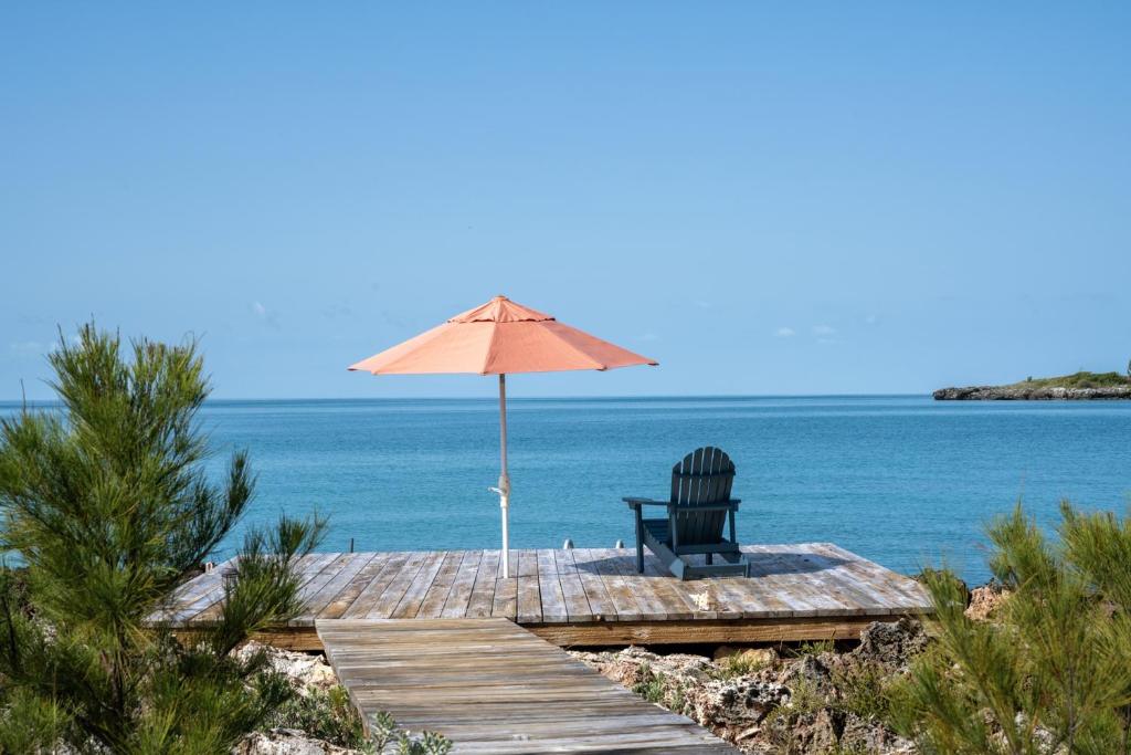 a chair sitting on a dock with an umbrella at Chez Cay Cottage cottage in Governorʼs Harbour
