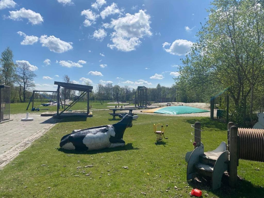 una estatua de una vaca yaciendo en la hierba en un parque en Pipowagens bij Pannenkoekenrestaurant & Camping De Koppenjan 'Een uniek verblijf met kinderspeelboerderij', en Jubbega-Schurega