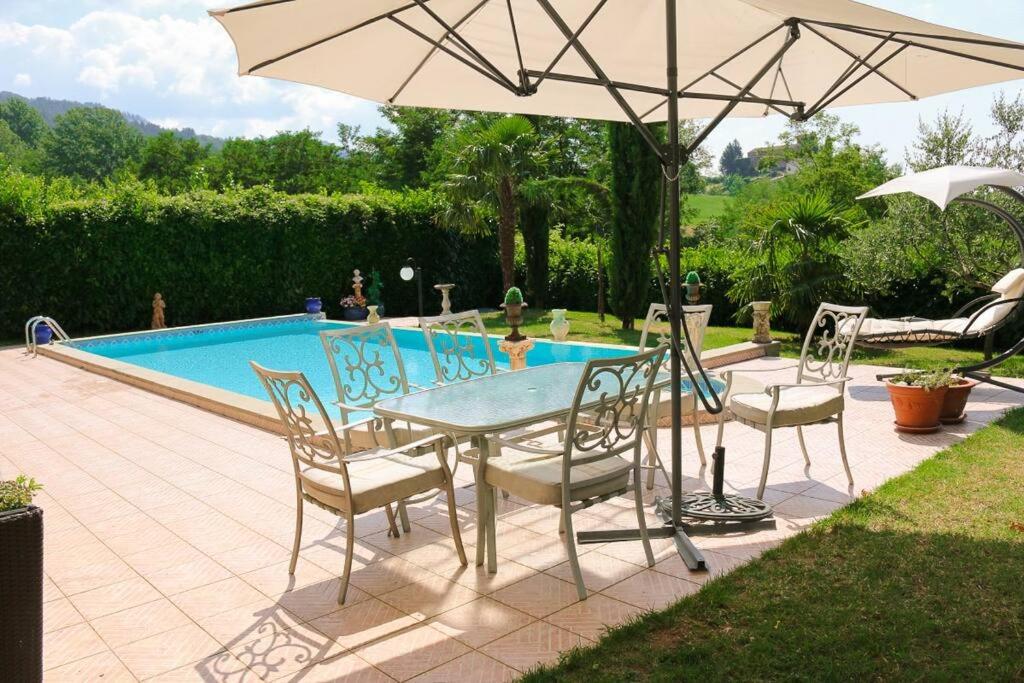 una mesa con sillas y una sombrilla junto a la piscina en Apartment at Villa Lorenzo, en Villa Collemandina