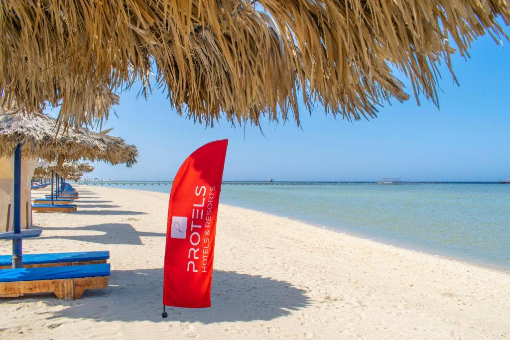 een rode surfplank op het strand onder een rieten parasol bij Protels Crystal Beach Resort in Marsa Alam