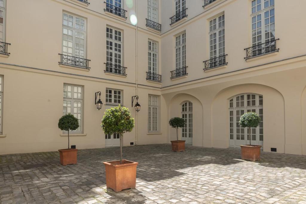 une cour avec trois arbres en pot devant un bâtiment dans l'établissement Spacious cocoon in the Marais, à Paris