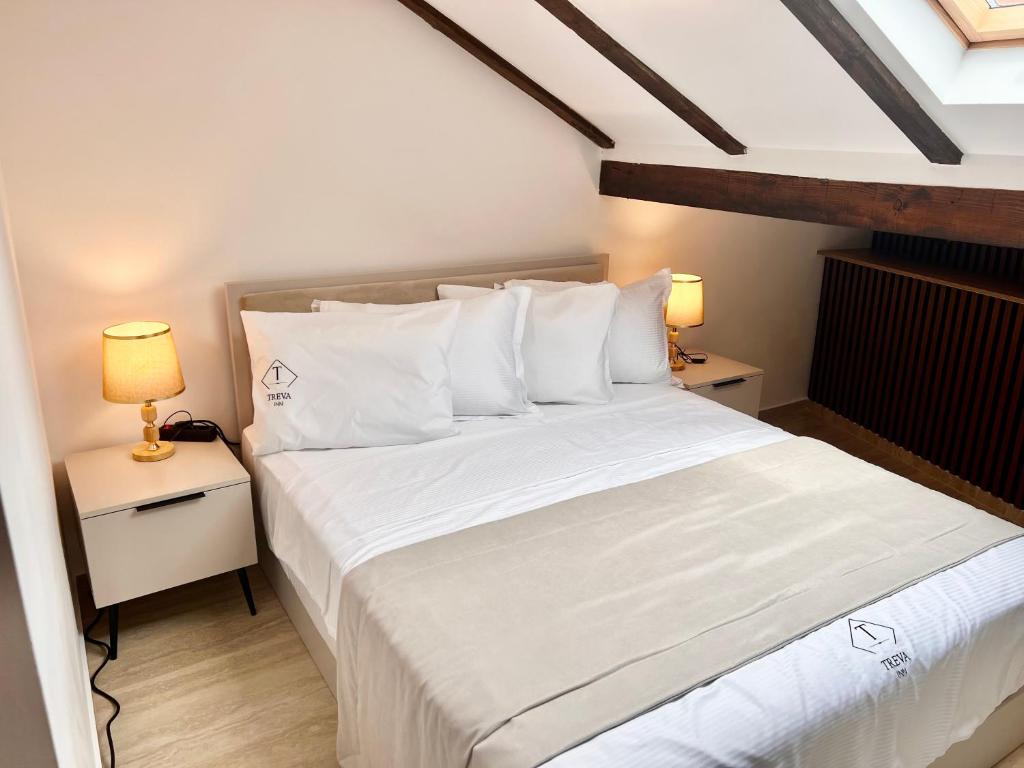 a bedroom with a bed with white sheets and two lamps at Treva Hotel in Prizren