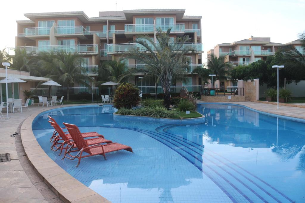 a swimming pool with two chairs and a building at PALM BEACH Porto das Dunas, apartamento TÉRREO confortável a 350 metros Beach Park in Aquiraz