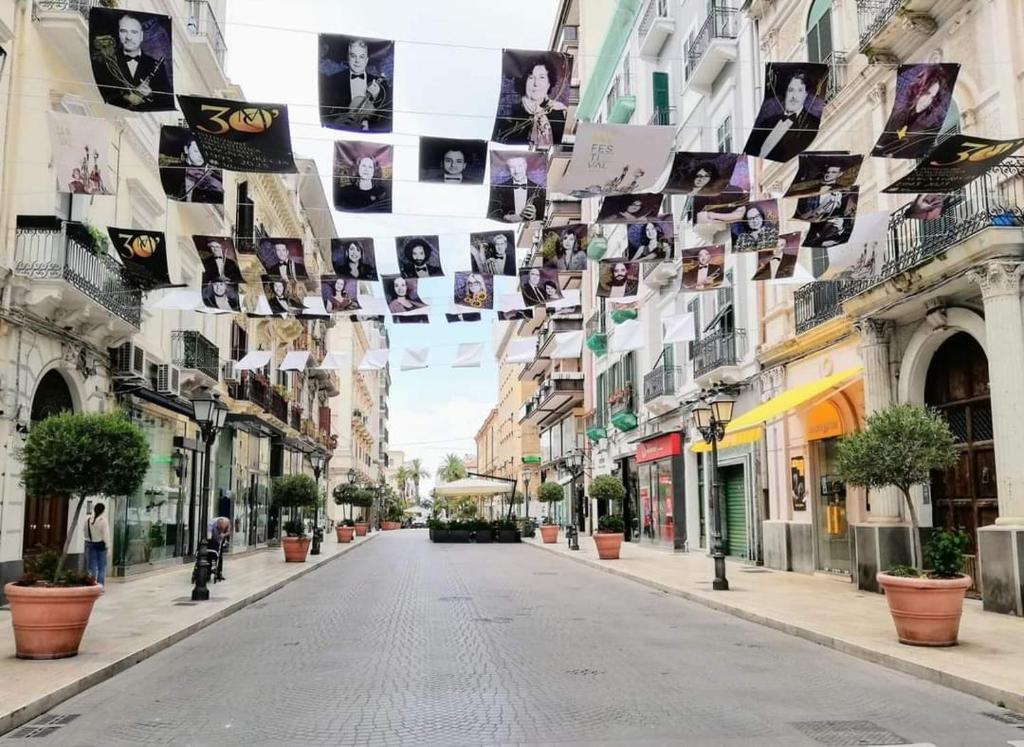 an empty street in a city with photos hanging from buildings at Sedici Scalini in Taranto