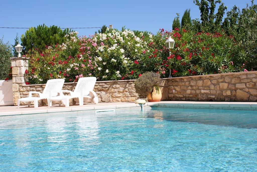 una piscina con 2 sillas blancas y flores en L’Olivier en Grignan
