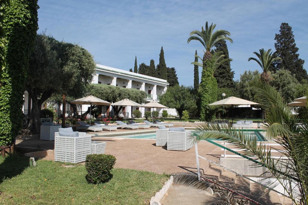 een resort met een zwembad met witte stoelen en parasols bij Hotel Transatlantique in Meknès