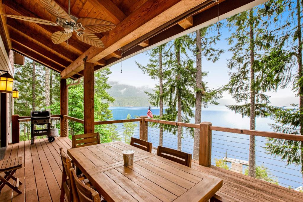 Un porche con una mesa y sillas de madera y una vista al agua. en Woodstone Cabin, en Hoodsport