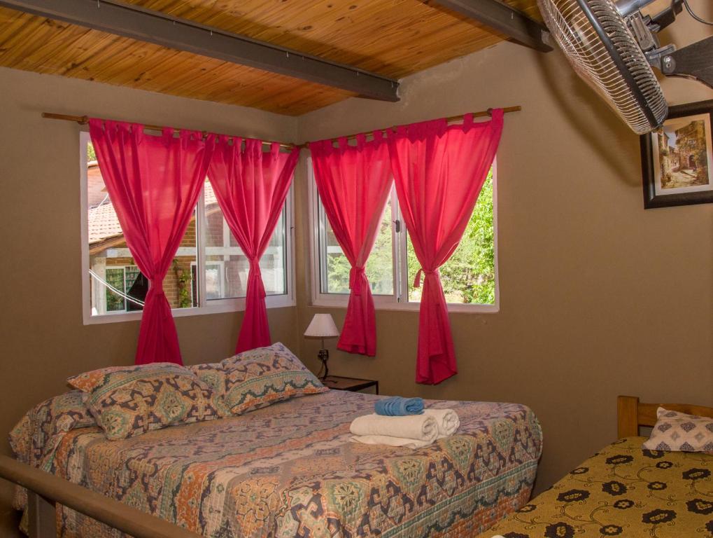 1 dormitorio con 1 cama y 2 ventanas con cortinas rojas en Un lugar en el mundo en Mina Clavero