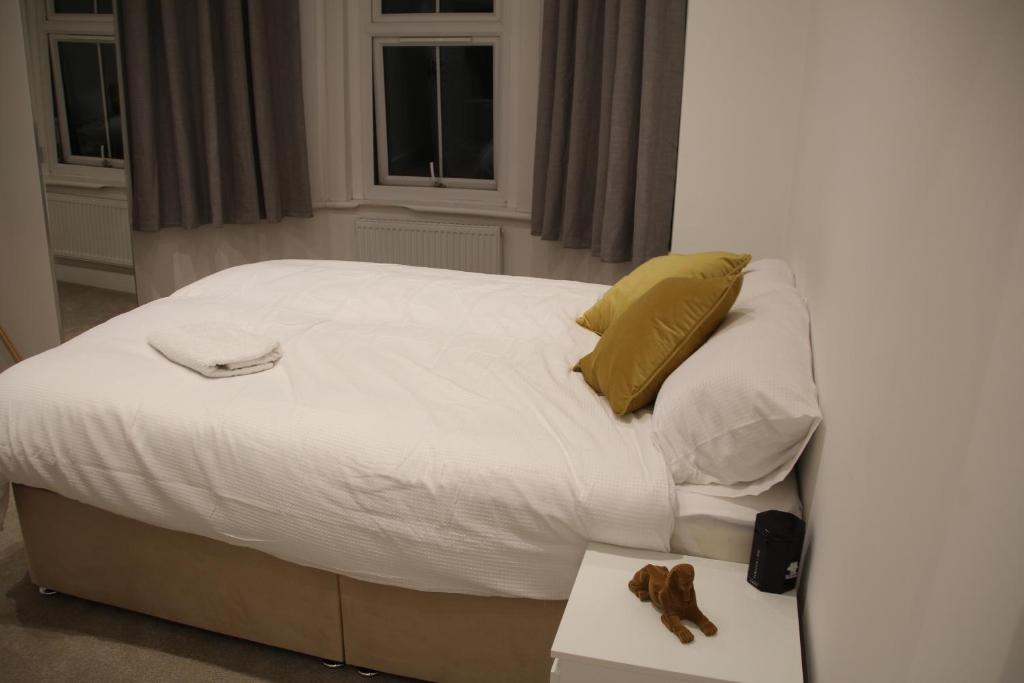 - un lit avec des draps blancs, des oreillers jaunes et une table dans l'établissement Comfortable Stone Bay window Private bathroom Ensuite Double Bedroom, à Edgware