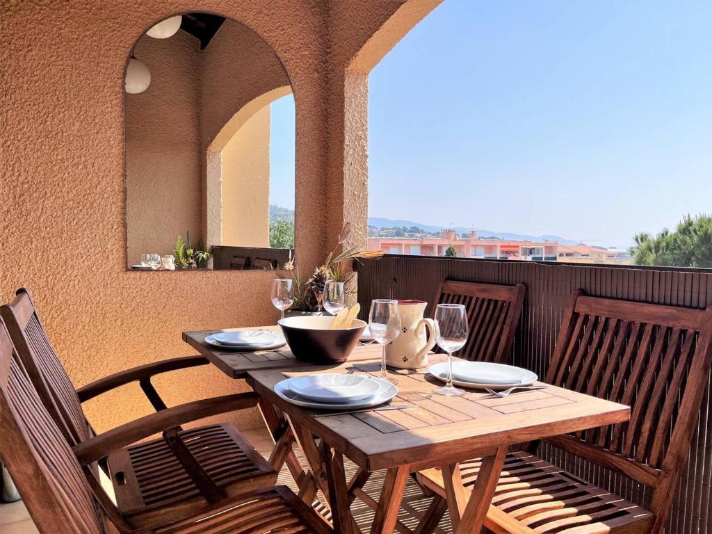 une table en bois avec des assiettes et des verres à vin sur un balcon dans l'établissement Studio avec terrasse, parking privé proche mer - FR-1-251-506, à Bormes-les-Mimosas