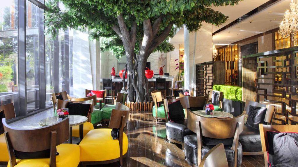 Holiday Inn Shanghai Hongqiao West, an IHG Hotel في Qingpu: مطعم بطاولات وكراسي وشجرة في الوسط