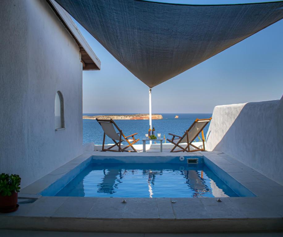a swimming pool with two chairs and a table and the ocean at Irenes View Apartments in Agia Irini Paros
