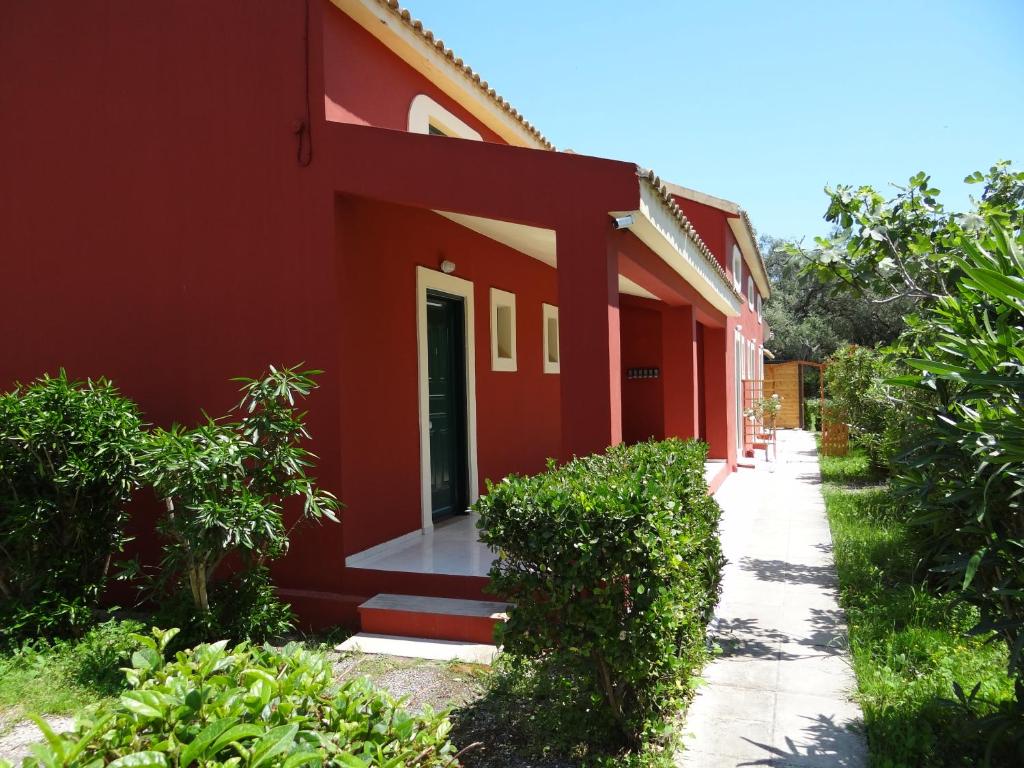 a red building with a door and a sidewalk at LEFKES Apartments Sidari in Sidari