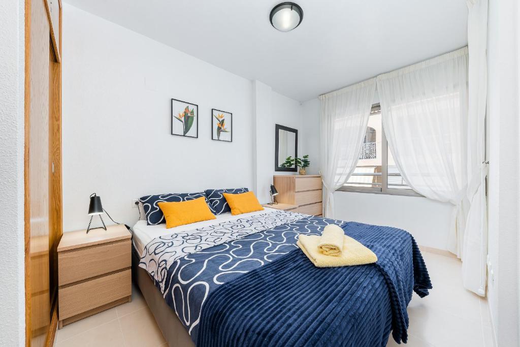 sypialnia z niebiesko-białym łóżkiem i oknem w obiekcie Apartament Playa de Los Locos w mieście Torrevieja
