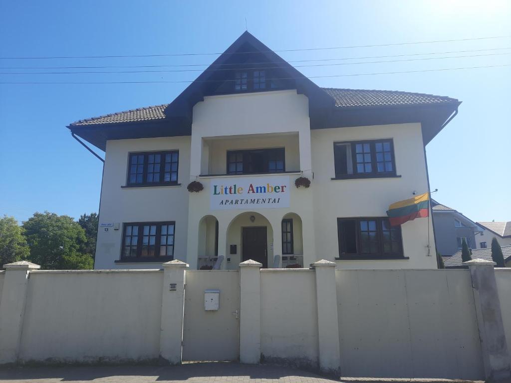 ein weißes Haus mit einem Zaun davor in der Unterkunft Little Amber Apartments in Klaipėda