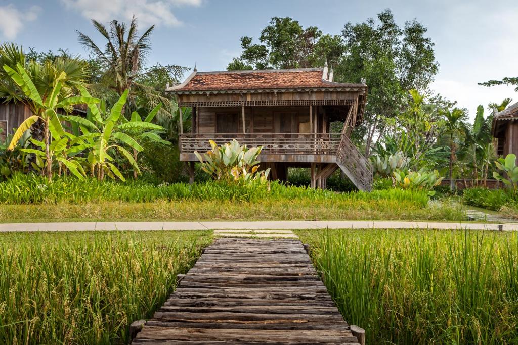 une passerelle en bois menant à une maison dans l'herbe dans l'établissement Sala Lodges, à Siem Reap