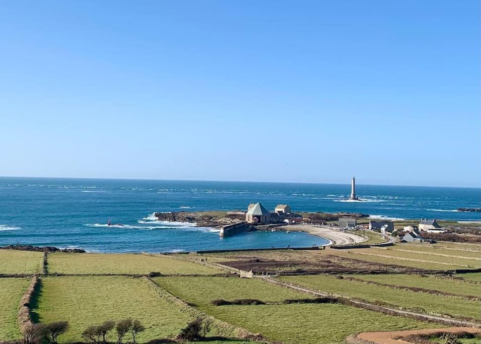 an island in the ocean with a lighthouse in the distance at Maison Bord de Mer dans la Petite Irlande in Auderville