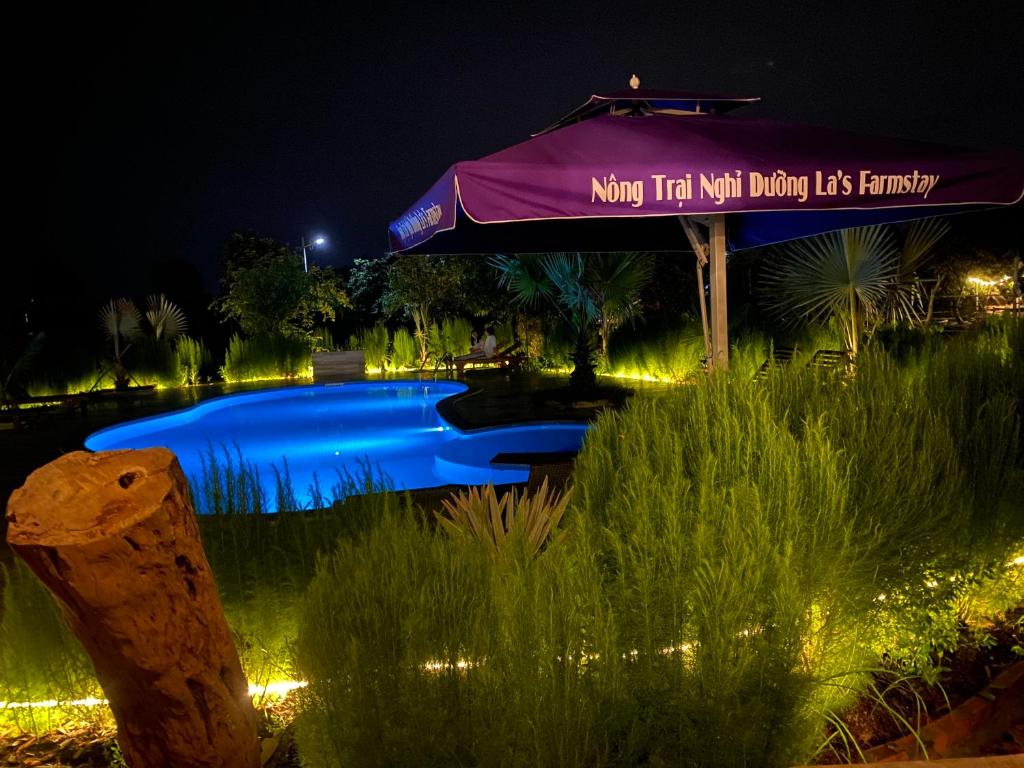 a swimming pool at night with a purple umbrella at LA'S FARMSTAY in Tây Ninh