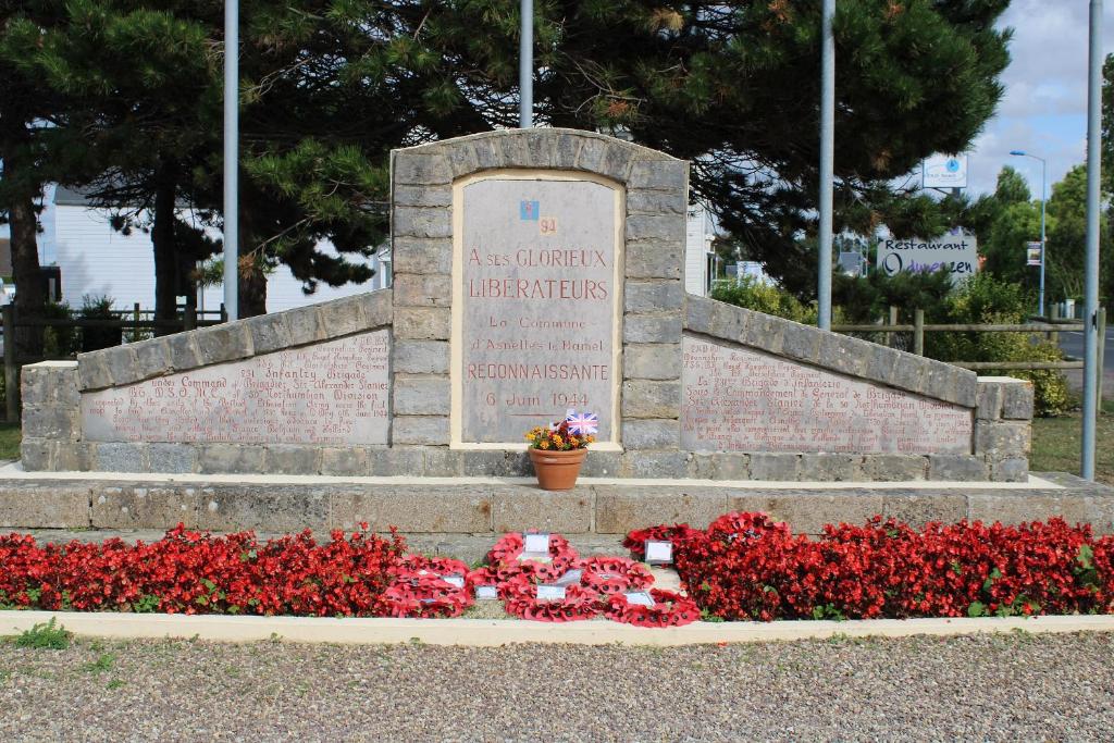 a war memorial with red flowers and a sign at La Fossette, maison neuve au coeur des plages in Asnelles
