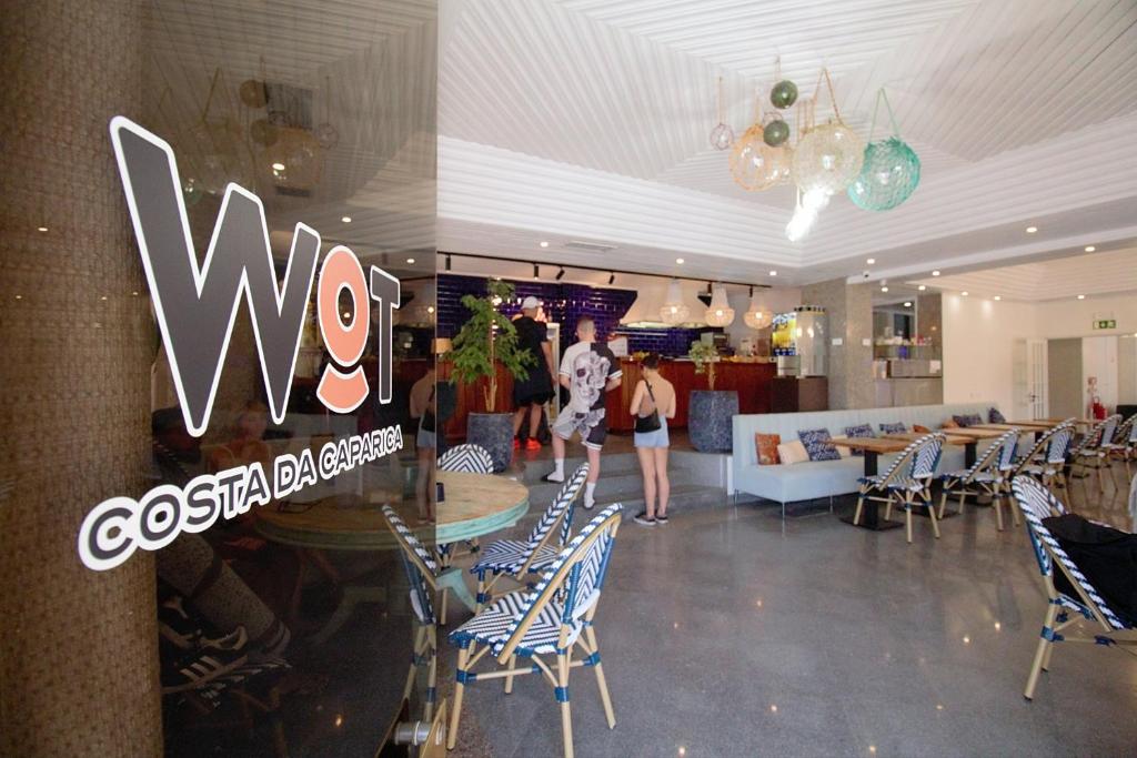 un restaurant avec un panneau lumineux sur le mur, des tables et des chaises dans l'établissement WOT Costa da Caparica, à Costa da Caparica