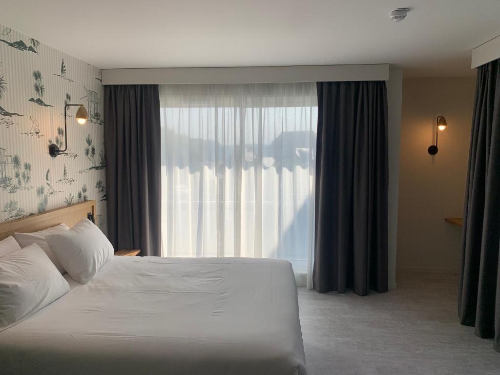 a bedroom with a bed and a large window at L'Escale Marine, The Originals Relais in Crozon