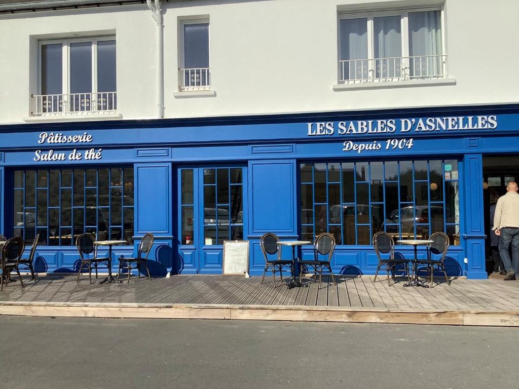 a blue building with chairs and tables in front of it at La Fossette, maison neuve au coeur des plages in Asnelles