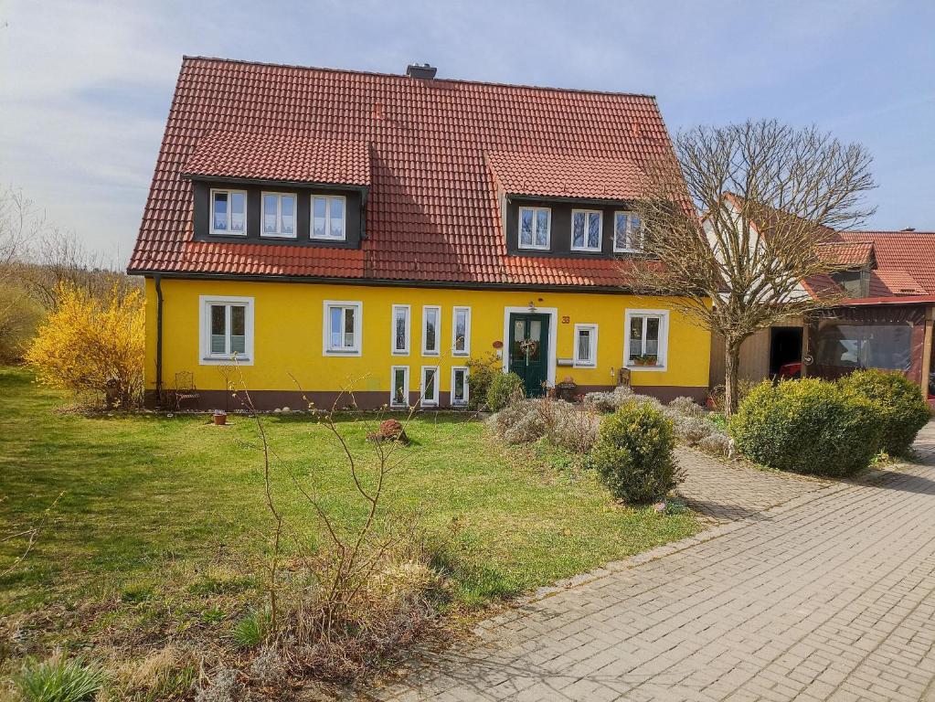 una casa amarilla con techo rojo en Ferienwohnung NatuRaum en Gräfenberg