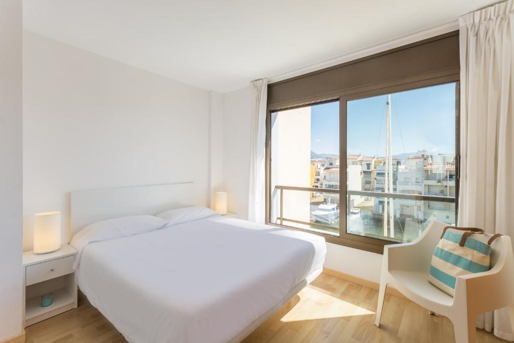 a white bedroom with a large bed and a large window at Pierre & Vacances Empuriabrava Marina in Empuriabrava