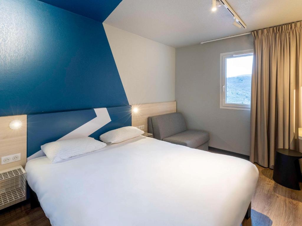 a bedroom with a white bed and a blue wall at ibis Budget Millau Viaduc in Millau