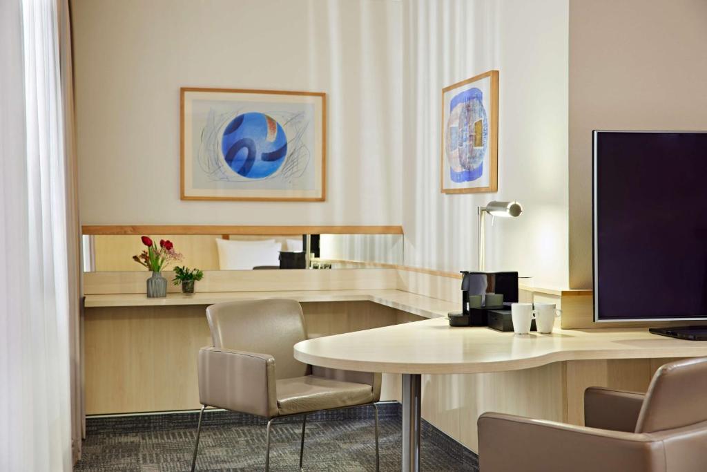 a hotel room with a desk with a monitor and chairs at Lindner Hotel Cologne Am Dom, part of JdV by Hyatt in Cologne