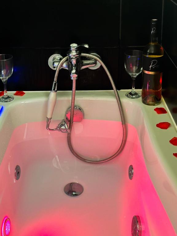 une baignoire rose avec un robinet et deux verres à vin dans l'établissement Golden Blue jacuzzi, à Annecy