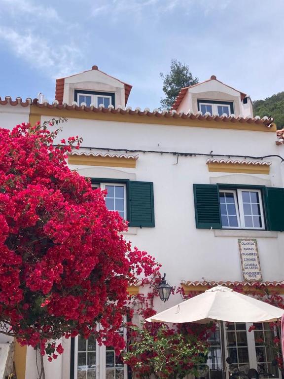 un edificio blanco con flores rojas y sombrilla en Casa da Nazaré, en Portinho da Arrábida