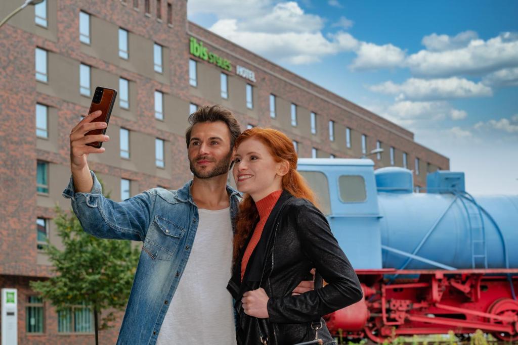 ibis Styles Hamburg Barmbek في هامبورغ: a man and a woman taking a picture with a cell phone