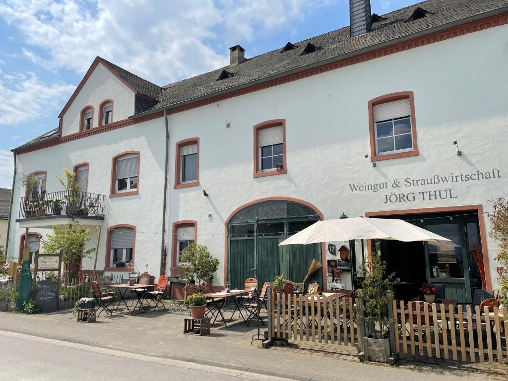 a white building with tables and chairs and an umbrella at Weingut und Gästezimmer Jörg Thul in Detzem