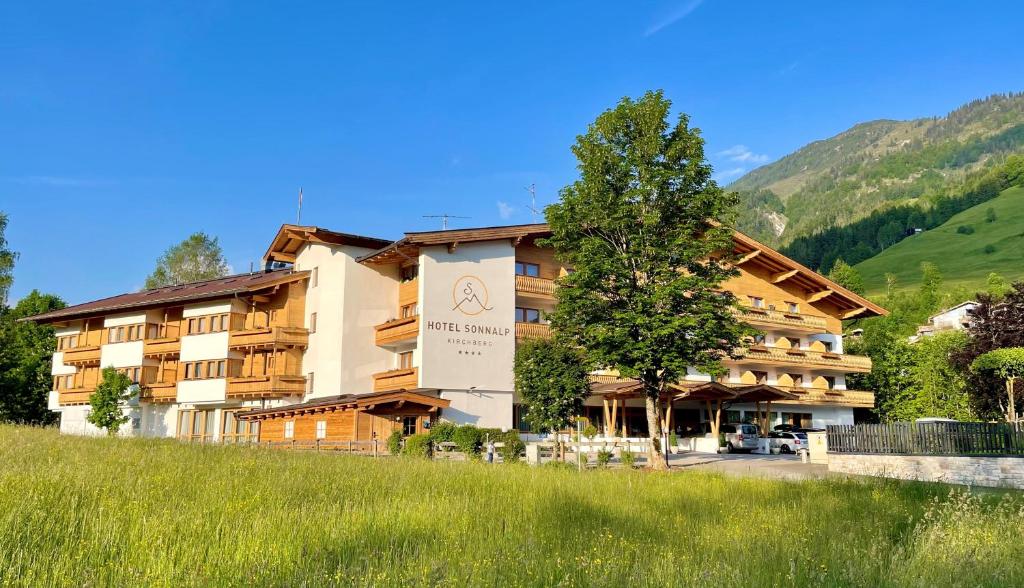 um hotel nas montanhas com uma árvore em primeiro plano em Hotel Sonnalp em Kirchberg in Tirol