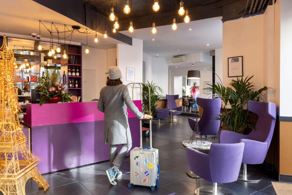 a woman walking with luggage in a restaurant with purple furniture at Avalon Hotel in Paris