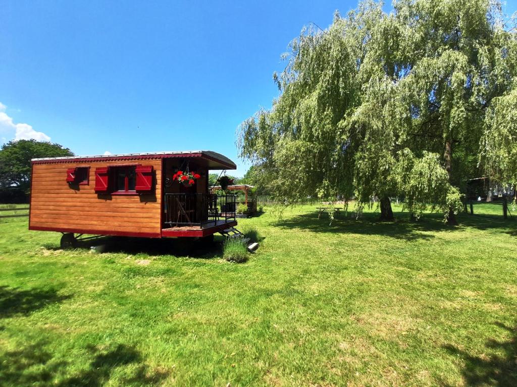 une petite maison dans un champ avec un arbre dans l'établissement Jolie roulotte au bord de la mare, à La Bretauche