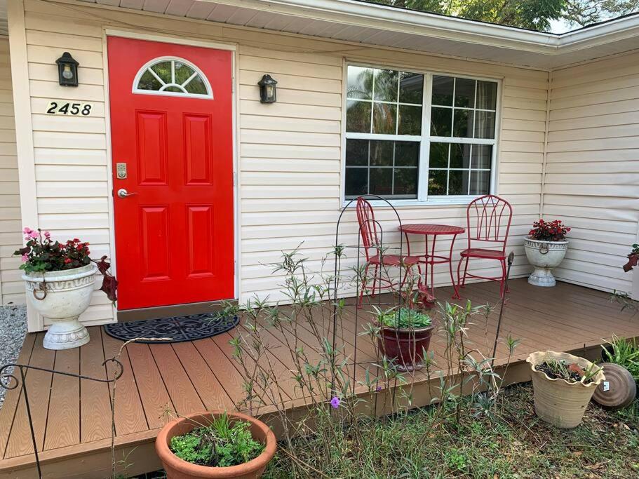 Cozy Cottage near Beaches and Downtown Sarasota في ساراسوتا: باب احمر على منزل به طاولة وكراسي