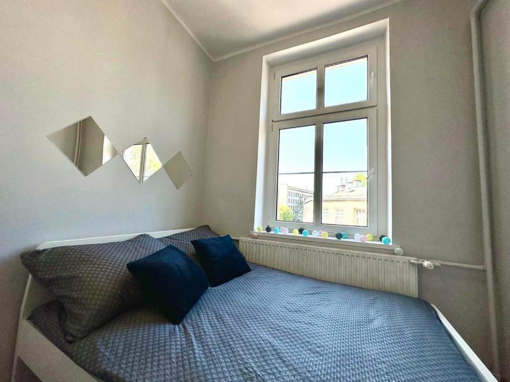 een slaapkamer met een bed met blauwe kussens en een raam bij MMRent One Way Room in Gdańsk
