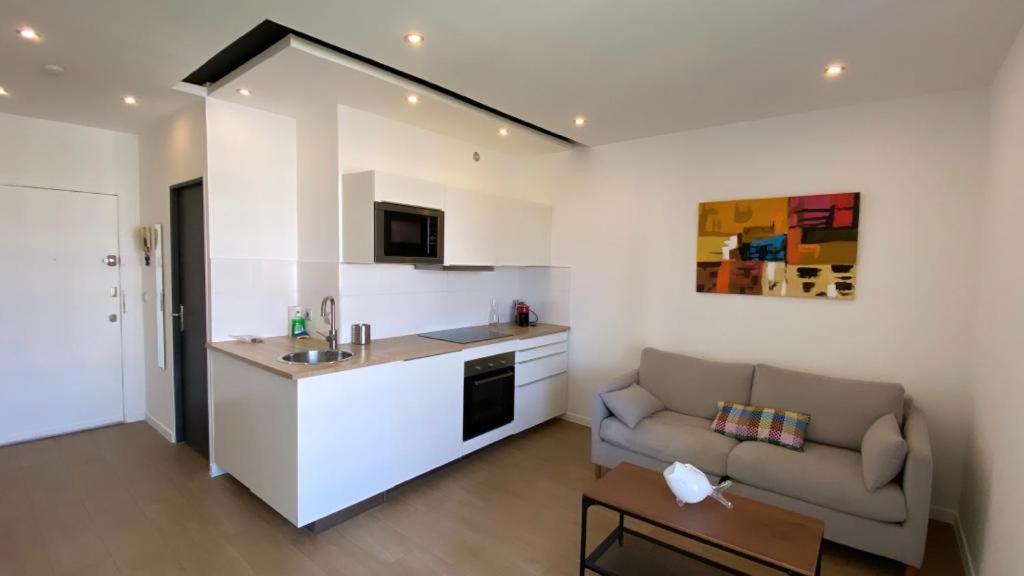ein Wohnzimmer mit einem Sofa und einer Küche in der Unterkunft Sublime Appart- Vue Mer-Prado13008- Proche Plage Vélodrome in Marseille