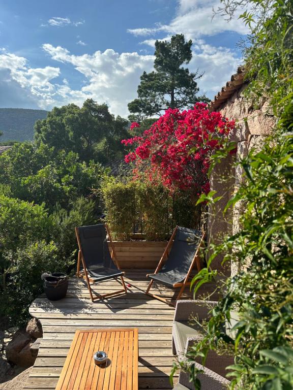 two chairs and a table on a wooden deck with flowers at Hôtel Ambassador Palombaggia in Porto-Vecchio