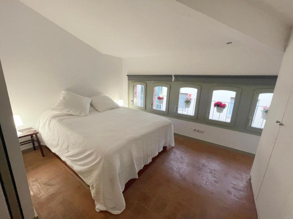 um quarto com uma cama com lençóis brancos e janelas em SG Apartamento céntrico ático em Terrassa