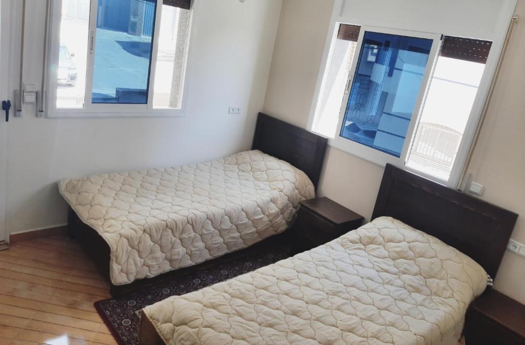 two beds in a room with two windows at Apartment pour les familles avec 2 chambres in Al Hoceïma