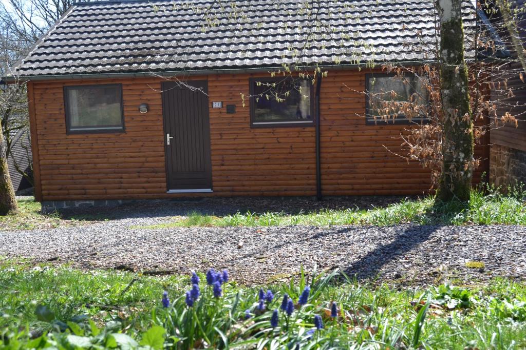 eine Holzhütte mit schwarzer Tür und ein paar Blumen in der Unterkunft L'Ard'Heure D'Avance in Somme-Leuze