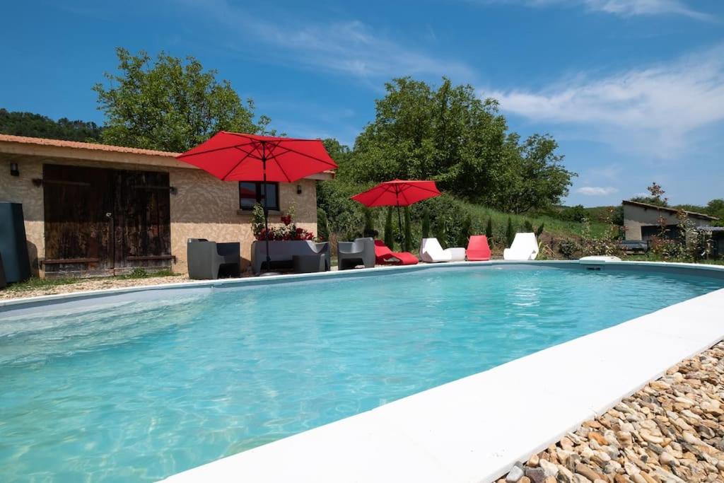 - une piscine avec des parasols et des chaises rouges dans l'établissement COMBE JOLIE Clim, Piscine & Jacuzzi, à Saint-Vincent-de-Cosse