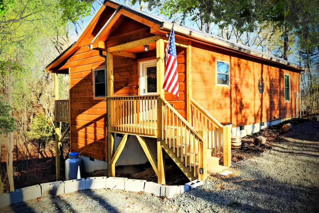 a wooden cabin with an american flag on the porch at New Serene, Fun & Comfy Cabin- Covered Deck, Grill, Arcade in Murphy