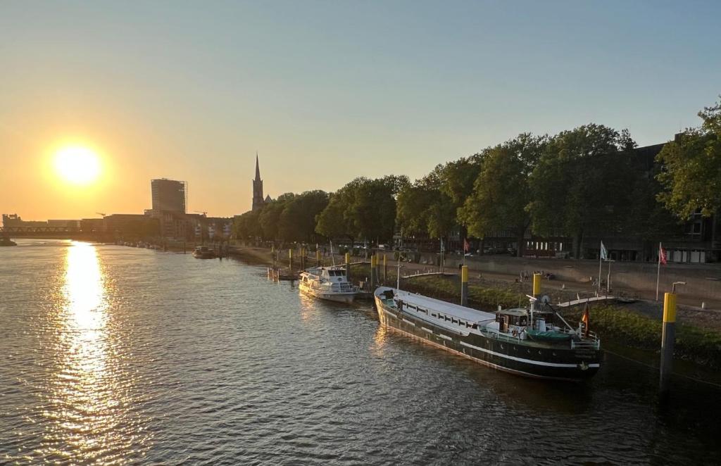 Zwei Boote sind bei Sonnenuntergang an einem Fluss angedockt. in der Unterkunft Küstenmotorschiff Aventura in Bremen