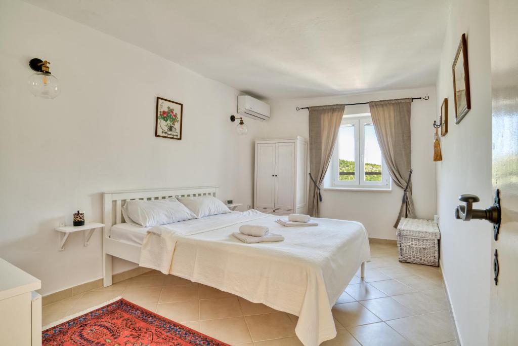 a white bedroom with a bed and a window at Eva's country house in Buljarica