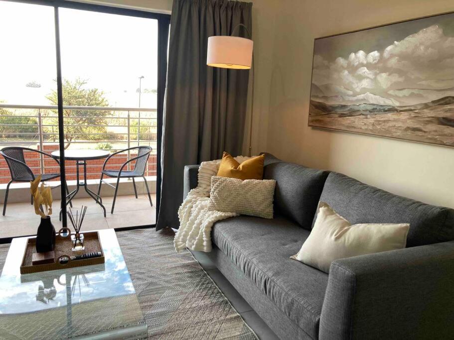 een woonkamer met een grijze bank en een balkon bij Luxury 1bed Serengeti OliveWood ORT Airport in Kempton Park